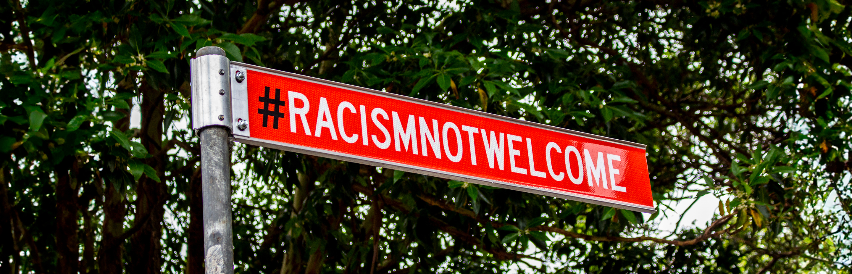 Red street sign that reads "Racism not welcome"