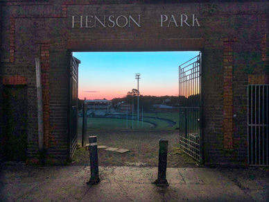 A brick gate with the text Henson Park on its top arch opens up to a vista of a sporting ground.
