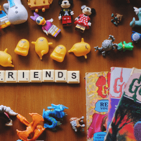 Small colourful plastic trinkets and toys and scrabble letters that spell 'friends on a table