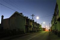 Darkened streetscape with streetlights powerlines and rows of two story historic terrace houses stretching along road from left foreground to right background