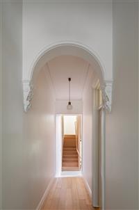 Interior hallway with heritage archway leading to stairs at end of hall along warm timber flooring