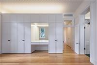 Interior space with warm timber floors tall white wardrobes with a small sitting area with mirror open door going off to the right and another door on the right leading down a hallway