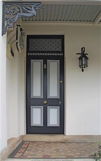 Image of outdoor entry area with white walls dark grey dragon truss feature and dark grey light fixture next to dark grey and light grey front door with yellow and red tiled flooring