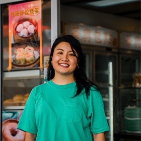 A woman in a green top stands in front of a dumpling restaurant