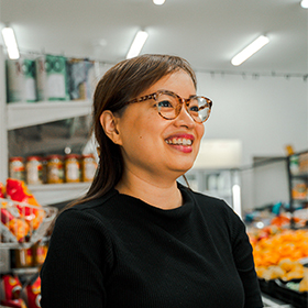 A woman with glasses and a black top stands in a fruit shop