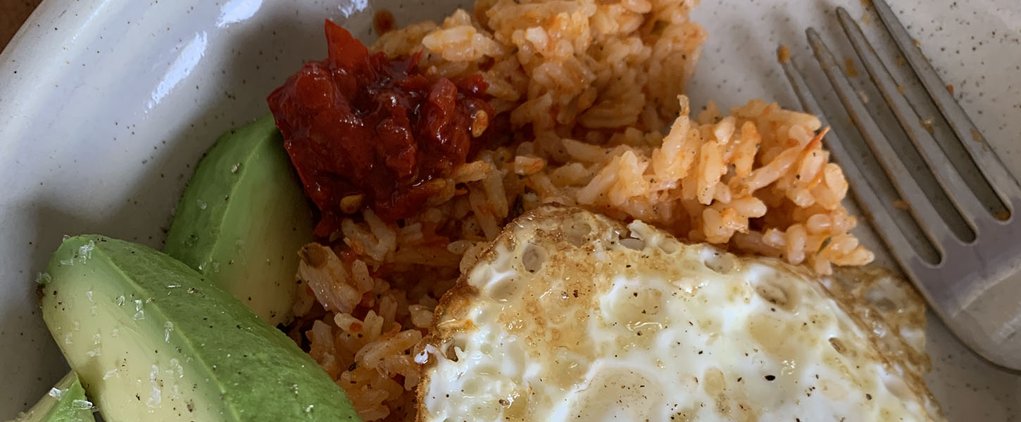 A snack-size meal of tomato rice with avocado and a fried egg on a small plate