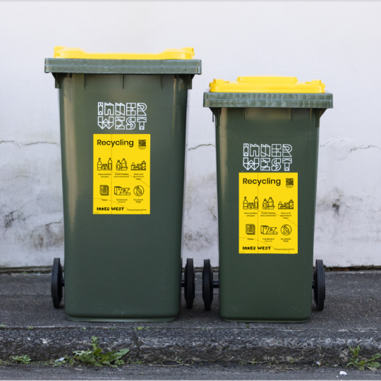 Two green garbage bins side by side with yellow sticked on the side