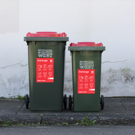 Two red lid bins side by side with a large rectangular red sticker on the front