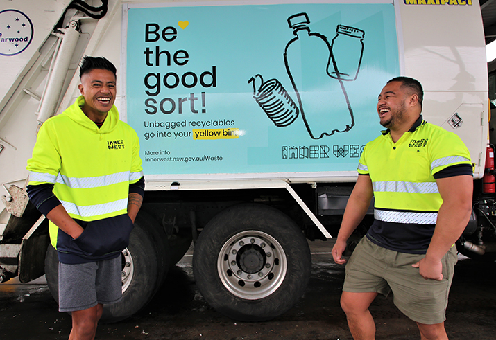 Two guys in front of the garbage truck with Be the good sort banner 