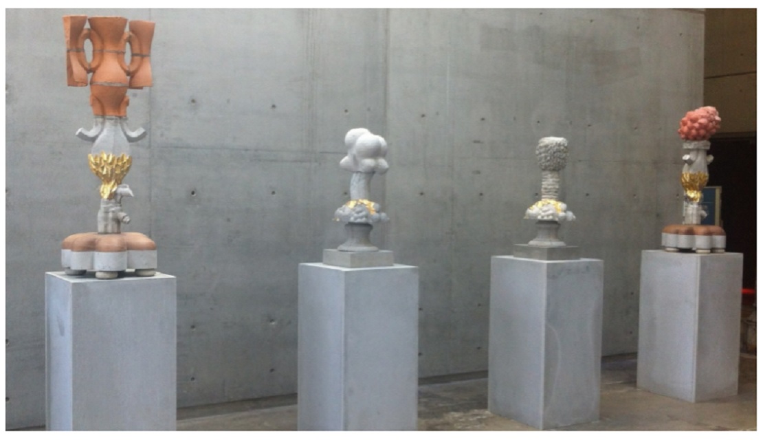 Photo of concrete plinths with 4 sculptures placed on top, the sculptures have organic round shapes and  are concrete grey, gold, orange and terracotta 