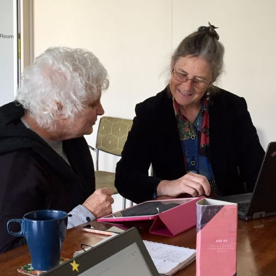 Two people sitting at a table using both a tablet device and a laptop