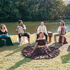four people sit on chairs in a field whilst a woman with a long skirt sits on the grass