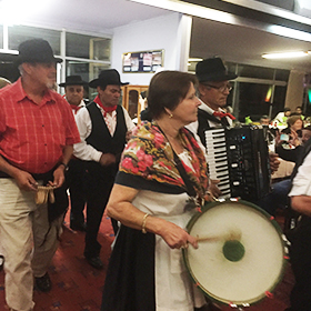 A woman in folk costume plays a drum with a group of people standing behind her