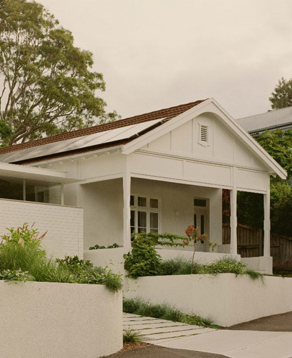 A diagonal front view of a white house with a verandah and a landscaped front yard