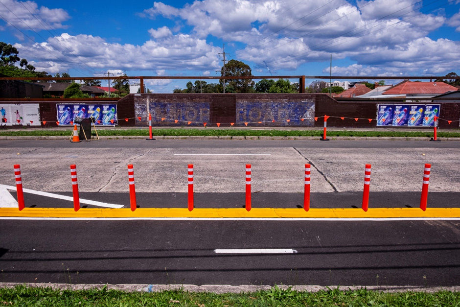 A perpendicular view from the middle of a road bridge in a residential area. A cycleway is in the foreground and there is construction bunting on the opposite side of the roadway.