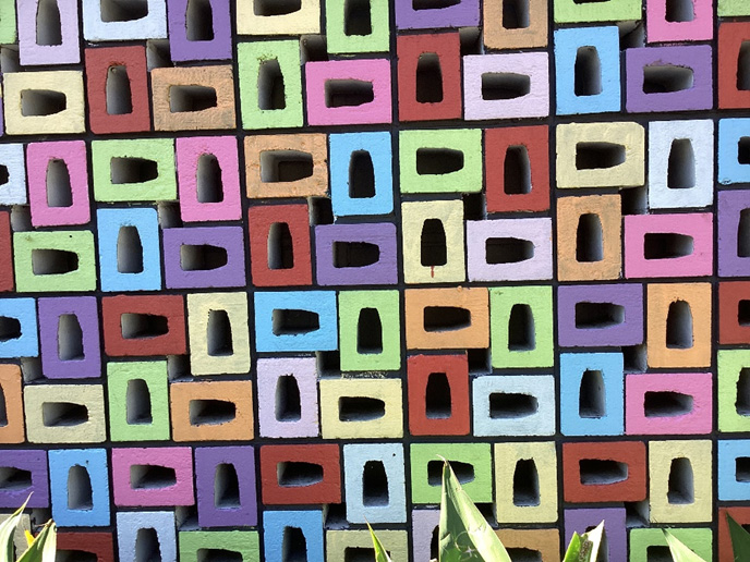 A wall of concrete bricks with the hollow centres exposed outwards. The bricks have been painted in alternating colours which emphasises the striking geometric pattern.