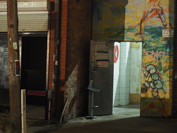 Light pours through an open door in the laneway of an urban factory district.