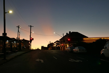 Sunset view of an urban street with terrace houses on the left side and a historic hotel on the right side.