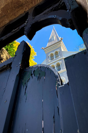 Peering through a wooden gate to reveal the tower structure on a distinctive old house.