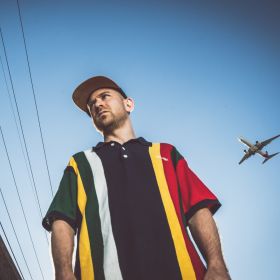 Portrait of Rapaport taken from low angle with plane in the sky