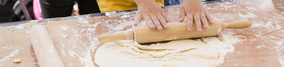 Childs hands rolling pizza dough on wooden table with wooden rolling pins