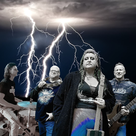 A four piece band pose with rock instruments against a story sky with bright white lightiening bolds shooting down behind them. On the left a man man sits at a drum kit, another has a tamborine around his neck. A woman holds a guitar upright and a man holds his bass horizontally