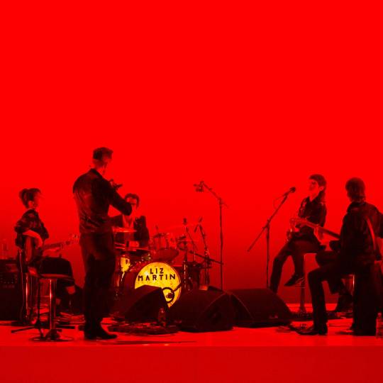 red background featuring 5 members of the band playing their instruments