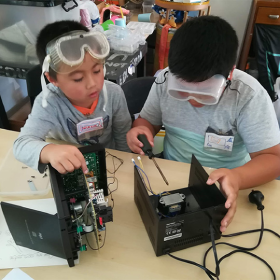 Two kids wearing goggles putting together electronic components 