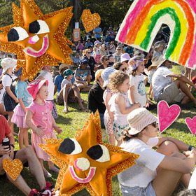 Kids and parents sitting in grass at a festival on a sunny day. Cutout rainbows and sparkly gold stars are scattered over parts of the image
