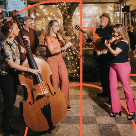 Group of musicians playing traditional instruments with fairylights in the background