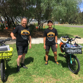 Two smiling people on a grassy area with bikes