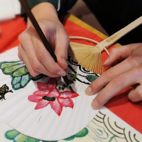 Person paining a flower on a white fan 
