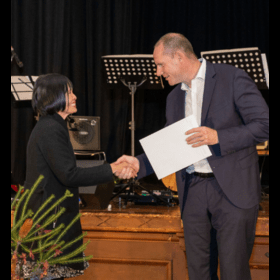 Two people on stage shaking hands, one is holding a certificate.