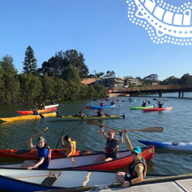 Kyaks in the water and a clear sunny day. People are smiling and holding their oars in the air