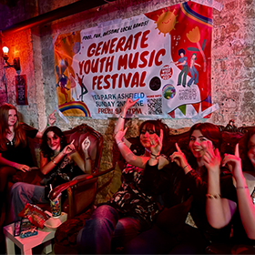 young people sitting on a couch with hands in the air in coloured lights