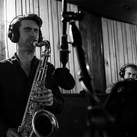 Black and while photo of a man soulfully playing a saxophone in front of a microphone