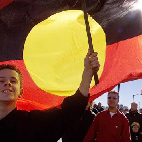 Boy stands proudly in front of the Aboriginal flag