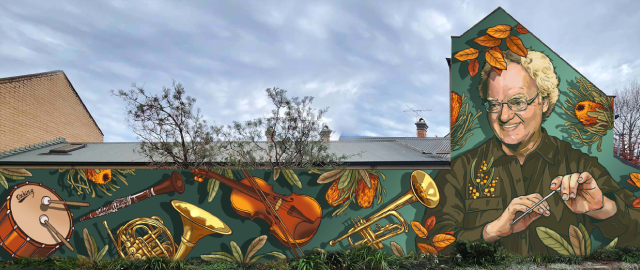 Mural painted on the side of a large house of musical instruments against a green background and a male conductor smiling holding a baton