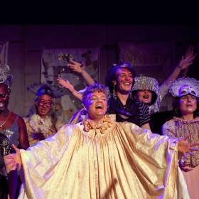 Group of performers singing in gaudy costumes with arms outstretched