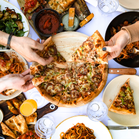 Close up of hands taking pizza slices from a table filled with delicious food