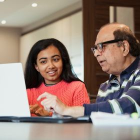 Teen girl helps senior man with computer