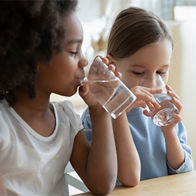Two girls sit in kitchen drink water_