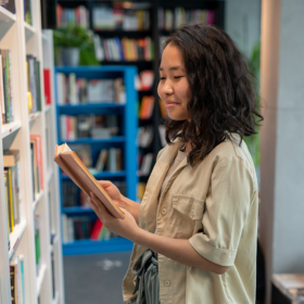 Young woman reading a book by a bookshelf
