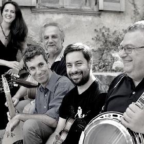 Black and white group photo of Greek folk rebetika 5 piece band Apodimi Compania, the five members all smile and look relaxed and 4 hold instruments, the fifth stands at the background, its a nice cheerful photo
