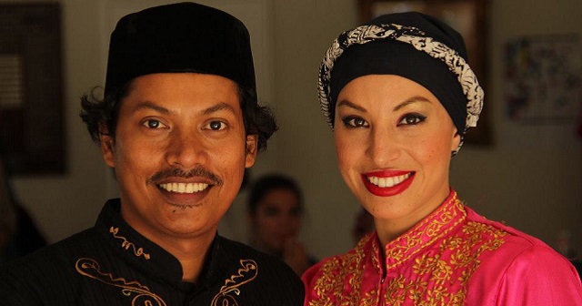 Beautiful; photo of Alfira and Bang smiling at camera, dancers are wearing traditional Indonesian costumes (shirts and hats/headdress). Head and shoulders shot only