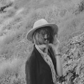Black and white photograph of singer Amber Rose in field wearing hat and peeping over sunglasses