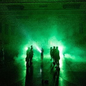 Photo of performers on timber flooring with green filtered light and bright white lights and torches shining