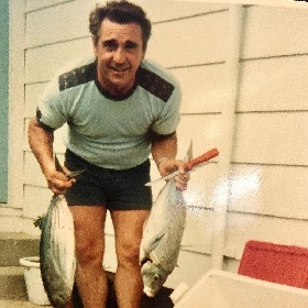 70s style photo of man wearing stubbies and t-shirt holding a large fish in each hand
