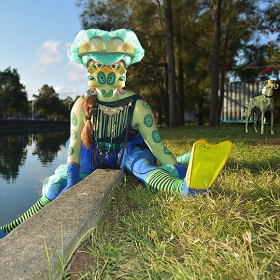 Photo of a person dressed up in flippers, stripey stockings, blue pants, body paint, face paint and headdress. The body paint is lime green with blue circular shapes