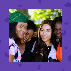 Photo of four young women smiling at camera, background blurred